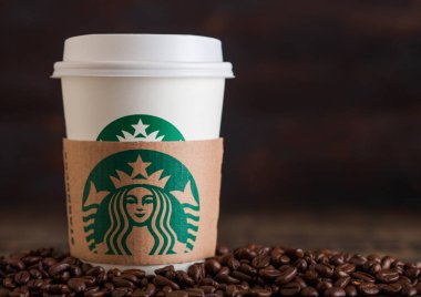 LONDON, UK - JUNE 05, 2019: Starbucks Coffee Paper Cup for take away with coffee beans on wooden background. Starbucks is the world's largest coffee house. clipart