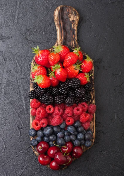 Fresh organic summer berries mix on vintage wooden chopping board black table background. Raspberries, strawberries, blueberries, blackberries and cherries.