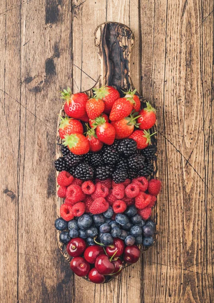 Fresh organic summer berries mix on vintage wooden chopping board on light wooden table background. Raspberries, strawberries, blueberries, blackberries.