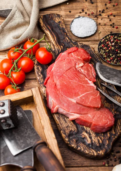 Fatia orgânica crua fresca de filé de bife refogado em tábua de cortar com garfo e faca em fundo de madeira. Cebola vermelha, tomates com sal e pimenta . — Fotografia de Stock