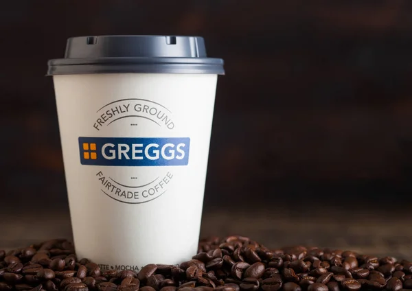 LONDRES, Reino Unido - 05 de junio de 2019: Greggs Coffee Paper Cup para llevar con granos de café sobre fondo de madera . — Foto de Stock