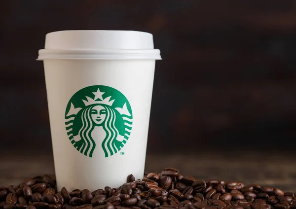 LONDRES, Reino Unido - 05 de junio de 2019: Starbucks Coffee Paper Cup para llevar con granos de café sobre fondo de madera. Starbucks es la cafetería más grande del mundo . — Foto de Stock