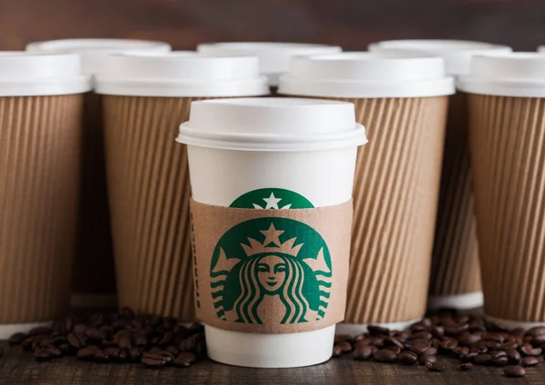 LONDRES, Reino Unido - 05 de junio de 2019: Starbucks Coffee Paper Cup para llevar con granos de café sobre fondo de madera con tazas de café en blanco . — Foto de Stock