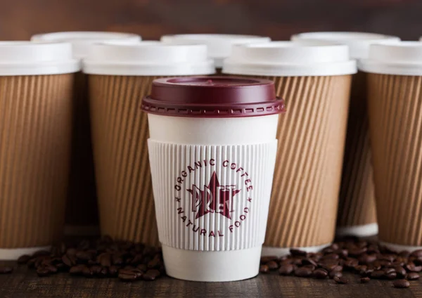 LONDRES, Reino Unido - 05 de junio de 2019: Pret A Manger Coffee Paper Cup para llevar con granos de café sobre fondo de madera con tazas de café marrón en blanco . — Foto de Stock