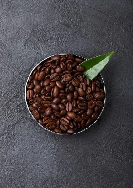Verse rauwe biologische koffiebonen in stalen kom met koffie TREA blad op zwarte achtergrond. — Stockfoto