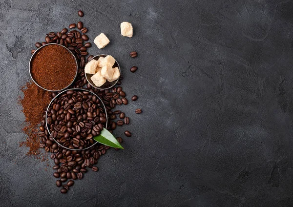 Fresh raw organic coffee beans with ground powder and cane sugar cubes with coffee trea leaf on black background. — Stock Photo, Image