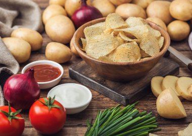 Taze organik ev yapımı patates ekşi krema ve kırmızı soğan ve ahşap masa arka plan üzerinde baharat ile ahşap kase cips cips. Ketçap ile taze sarı patates