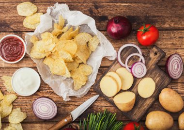 Taze organik ev yapımı patates cips ekşi krema ve kırmızı soğan ve baharat ahşap arka plan üzerinde cips. Doğrama tahtasında taze sarı patates ile.