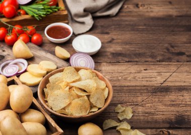 Taze organik ev yapımı patates ekşi krema ve kırmızı soğan ve ahşap masa arka plan üzerinde baharat ile ahşap kase cips cips. Ketçap ile taze sarı patates