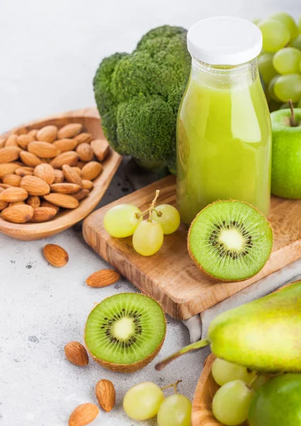 Taze smoothie suyu organik yeşil tonda meyve ve sebze taş mutfak arka plan üzerinde Cam şişe. Kasede badem fıstığı ile.