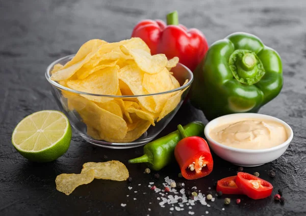 Prato tigela de vidro com batatas fritas batatas fritas com sabor de cebola no fundo da mesa de pedra preta. Pimentos de pimenta vermelha e verde com limão e molho picante quente com páprica . — Fotografia de Stock