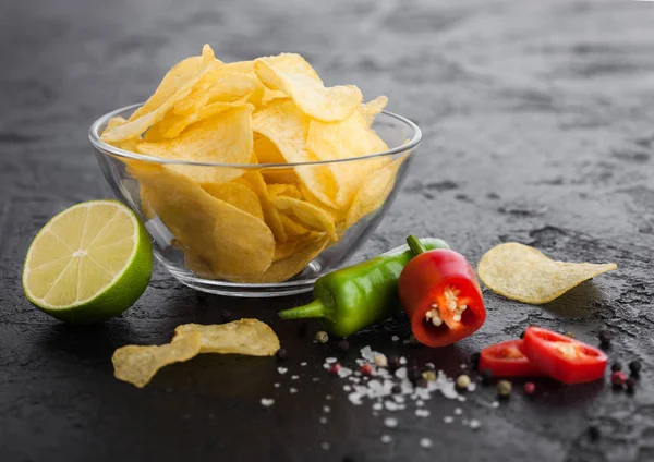 Placa de vidrio con patatas fritas con sabor a cebolla sobre fondo de mesa de piedra negra. Chiles rojos y verdes con limón y salsa picante picante . — Foto de Stock