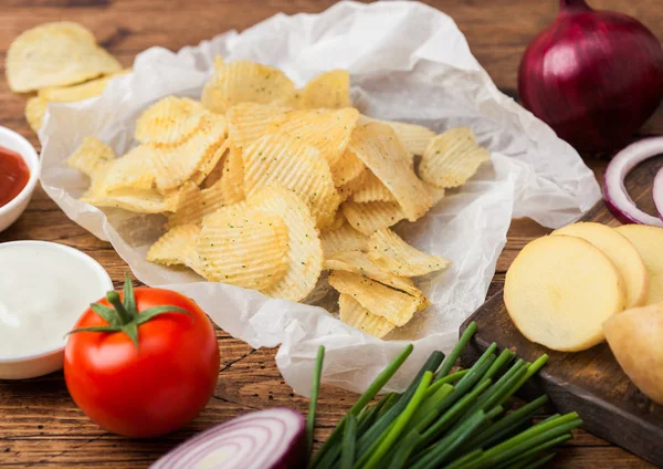 Patatas fritas frescas orgánicas caseras con crema agria y cebollas rojas y especias sobre fondo de madera. Con papas amarillas frescas y cebolla verde — Foto de Stock