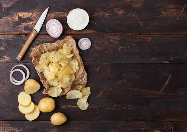 Patatas fritas frescas orgánicas caseras con crema agria y cebollas rojas sobre papel sobre fondo de madera oscura . — Foto de Stock