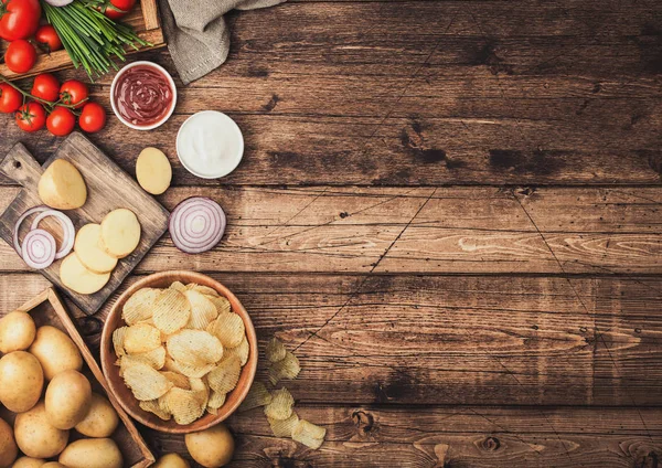 Fresh organic homemade potato crisps chips in wooden bowl with sour cream and red onions and spices on wooden table background. Top view.Fresh yellow potatoes with ketchup — Stock Photo, Image