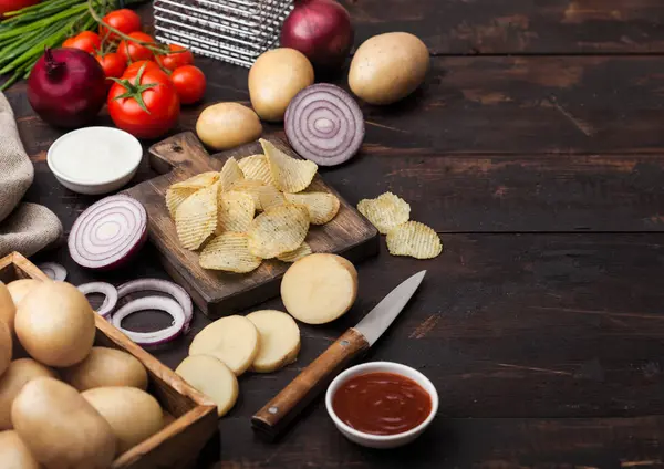 Patatas fritas frescas orgánicas caseras con crema agria y cebollas rojas sobre tabla de cortar sobre fondo de madera oscura. Tomates con cebolla verde y tazón de ketchup . — Foto de Stock