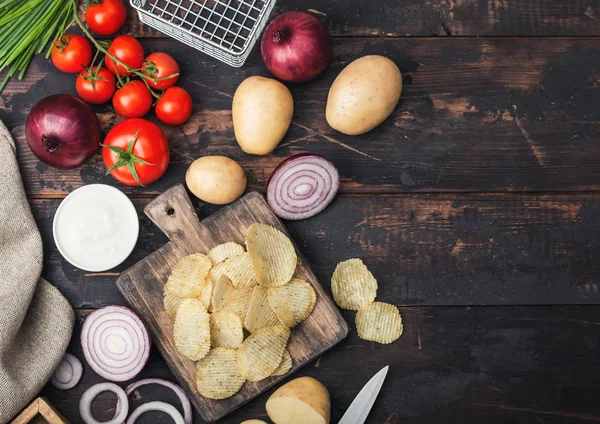 Patatas fritas frescas orgánicas caseras con crema agria y cebollas rojas sobre tabla de cortar sobre fondo de madera oscura. Tomates con cebolla verde y tazón de ketchup . — Foto de Stock