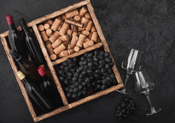 黒い石の背景にヴィンテージの木製の箱の中にコルクとオープナーと暗いブドウと赤ワインと空のグラスのミニボトル。トップビュー — ストック写真