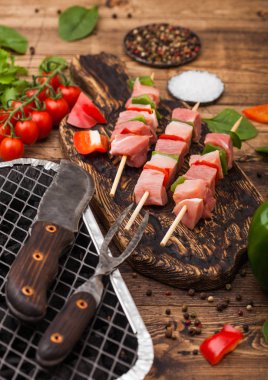 Çatal ve bıçak ile ahşap arka planda taze sebzeler ile tek kullanımlık kömür BBQ ızgara üzerinde Paprika ile ham domuz kebap. Tuz ve biber ile marul ve Paprika ve kiraz domates. Üst görünüm
