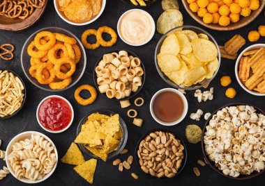 Fıstık, patlamış mısır ve soğan halkaları ve siyah arka planda kase plakaları tuzlu kraker ile tüm klasik patates atıştırmalıkları. Cips ve patates cipsi, nachos ve peynir topları ile cipsler ile Twirls.