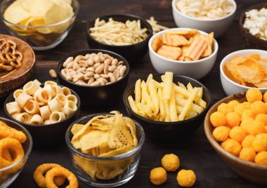 Tüm klasik patates atıştırmalıkları, fıstık, patlamış mısır ve soğan halkaları ve ahşap arka planda kase plakaları tuzlu kraker. Cips ve patates cipsi, nachos ve peynir topları ile cipsler ile Twirls.