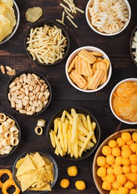 Tüm klasik patates atıştırmalıkları, fıstık, patlamış mısır ve soğan halkaları ve ahşap arka planda kase plakaları tuzlu kraker. Cips ve patates cipsi, nachos ve peynir topları ile cipsler ile Twirls.