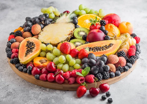 Čerstvé syrové organické letní bobule a exotické plody v kulaté velké tácu na pozadí s lehkou kuchyní. Papaya, hrozny, nektarinky, pomeranč, malinový, kiwi, jahoda, lycheky, třešeň a ananas. — Stock fotografie