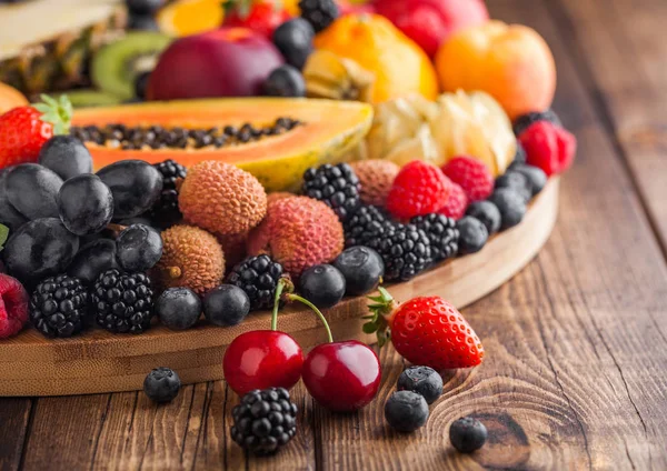 Frescas bayas de verano orgánicas crudas y frutas exóticas en bandeja redonda grande sobre fondo de cocina de madera. Papaya, uvas, nectarina, naranja, frambuesa, kiwi, fresa, lichis, cereza. Macro — Foto de Stock