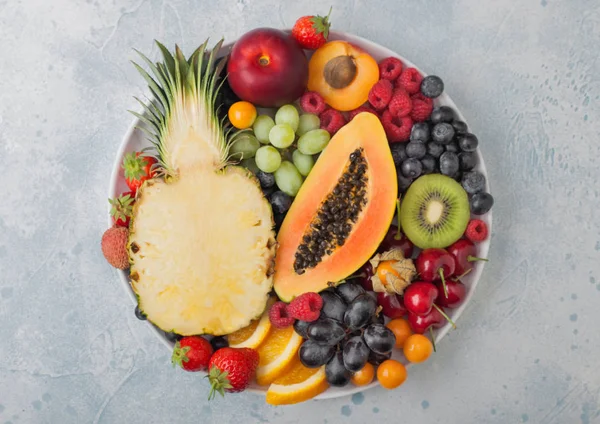 Frescas bayas de verano orgánicas crudas y frutas exóticas en plato blanco sobre fondo claro. Piña, papaya, uvas, nectarina, naranja, albaricoque, kiwi, pera, lichis, cereza y physalis . — Foto de Stock