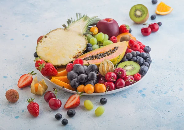 Frescas bayas de verano orgánicas crudas y frutas exóticas en plato blanco sobre fondo de cocina azul. Piña, papaya, uvas, nectarina, naranja, albaricoque, kiwi, pera, lichis, cereza y physalis . — Foto de Stock