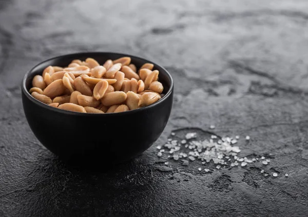 Gesalzene und geröstete Erdnüsse klassischer Snack in schwarzer Schüssel auf schwarzem Hintergrund. — Stockfoto