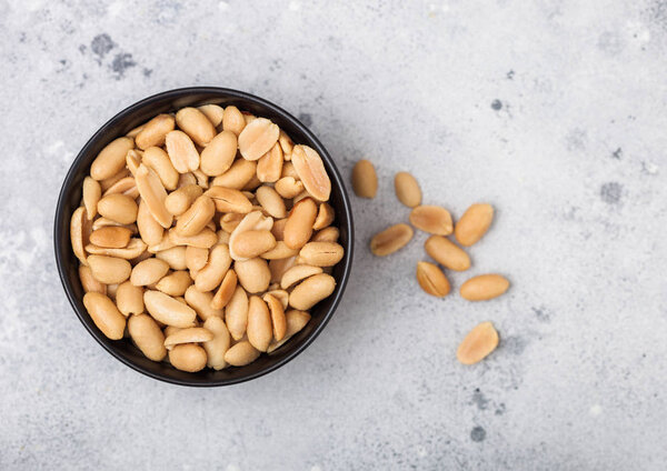 Salted and roasted peanuts classic snack in black bowl on light background.