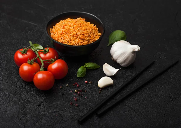 Black plate bowl of rice with tomato and basil and garlic and chopsticks on black stone background. Traditional food. — Stock Photo, Image