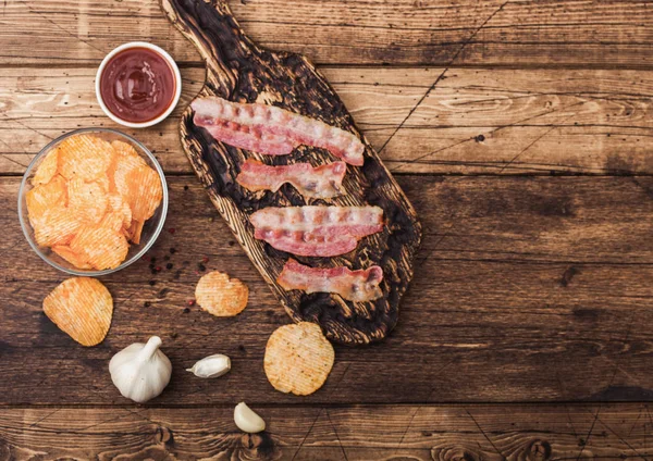 Patatas fritas con sabor backon con rashers de tocino a la parrilla sobre tabla de cortar vintage con ajo y salsa sobre fondo de madera . — Foto de Stock