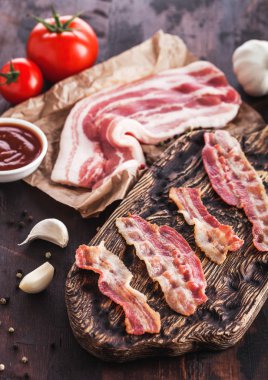 Sarımsak ve domates ile ahşap tahta üzerinde kasaplar kağıt üzerinde ham taze füme domuz pastırması ile vintage ahşap tahta üzerinde Izgara pastırma şeritler.