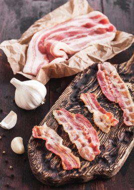 Sarımsak ile ahşap tahta üzerinde et balta ile kasaplar kağıt üzerinde çiğ taze füme domuz pastırması ile vintage ahşap tahta üzerinde Izgara pastırma şeritler.