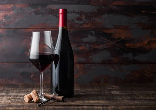 Elegante bicchiere e bottiglia di vino rosso con tappi e cavatappi su fondo in legno scuro. Luce naturale — Foto Stock