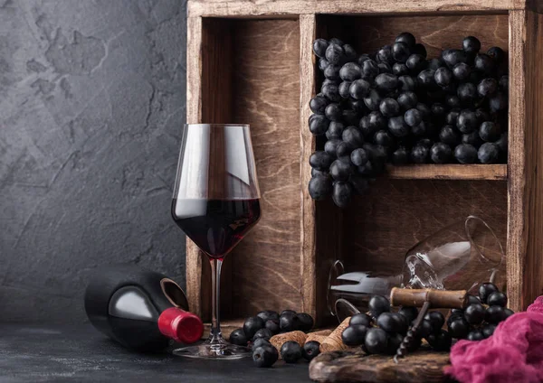 Rotweinflaschen mit dunklen Trauben in einer Holzkiste auf schwarzem Steinhintergrund. elegantes Weinglas mit Korken und Korkenzieher auf schwarzem Brett. Tageslicht — Stockfoto