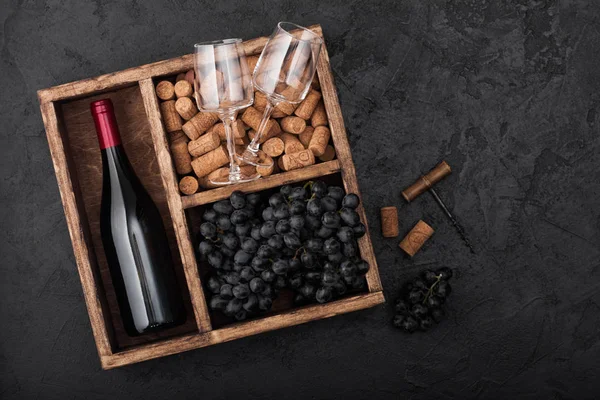 Bouteille de vin rouge et verres vides avec raisins noirs avec bouchons et ouvre-bouteille à l'intérieur boîte en bois vintage sur fond de pierre noire. Vue du dessus — Photo