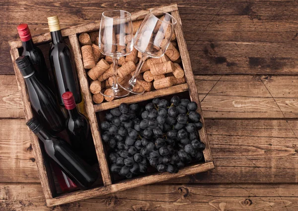 Mini bottles of red wine and empty glasses with dark grapes with corks and opener inside vintage wooden box on grunge wooden background. Top view