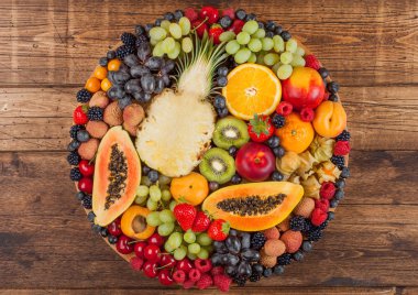 Ahşap mutfak arka plan üzerinde yuvarlak büyük tepsitaze ham organik yaz meyveleri ve egzotik meyveler. Papaya, üzüm, nektarin, portakal, ahududu, kivi, çilek, lychees, kiraz. 