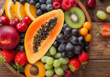 Ahşap mutfak arka plan üzerinde yuvarlak ahşap tabak taze ham organik yaz meyveleri ve egzotik meyveler. Papaya, üzüm, nektarin, portakal, ahududu, kivi, çilek, lychees, kiraz. Makro