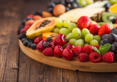 Ahşap mutfak arka plan üzerinde yuvarlak büyük tepsitaze ham organik yaz meyveleri ve egzotik meyveler. Papaya, üzüm, nektarin, portakal, ahududu, kivi, çilek, lychees, kiraz. Makro