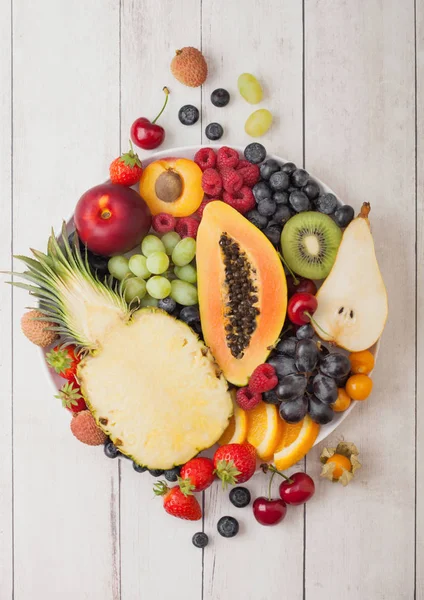 新鲜的生有机夏季浆果和异国情调的水果在白色木背景的白色板。菠萝，木瓜，葡萄，花蜜，橙子，杏，奇异果，梨，芦荟，樱桃和香菜. — 图库照片
