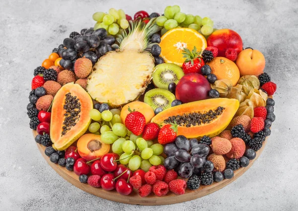 Friss nyers bio nyári bogyók és egzotikus gyümölcsök kerek nagy tálcában, világos konyhás háttérrel. Papaya, szőlő, nektarin, narancs, málna, Kiwi, eper, lychees, cseresznye és ananász. — Stock Fotó