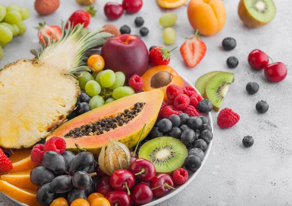 Свежие органические летние ягоды и экзотические фрукты в белой тарелке на светлом фоне. Ананас, папайя, виноград, нектарин, апельсин, абрикос, киви, груша, личи, вишня и физалис. Макро — стоковое фото