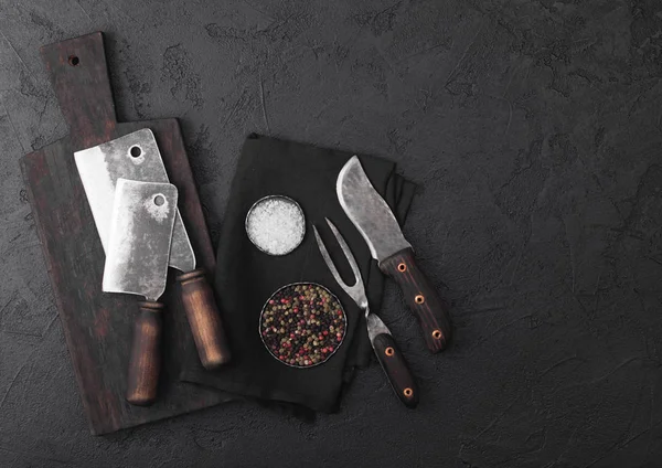 Cuchillo de carne vintage y tenedor y hachas con tabla de cortar vintage y fondo de mesa negro. Utensilios de carnicero. Sal y pimienta — Foto de Stock