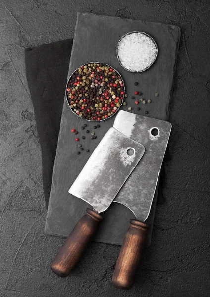 돌 도마와 검은 테이블 배경 빈티지 고기 칼 도끼입니다. 정육점 기구. 소금과 후추. — 스톡 사진