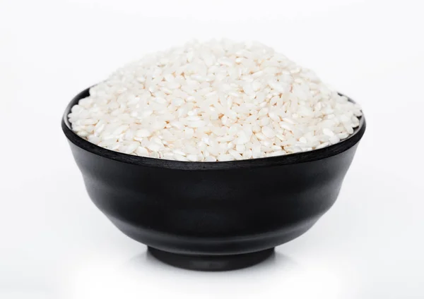 Black bowl of raw organic arborio risotto rice on white background. Healthy food. — Stock Photo, Image