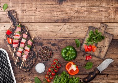 Çatal ve bıçak ile ahşap arka planda taze sebzeler ve tek kullanımlık kömür ızgara ile doğrama tahtasında Paprika ile ham domuz kebap. Tuz ve biber, marul ve Paprika. Üst görünüm